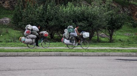 PYNCTM 09/07/2018, Kaesong, North-Korea: two hopeless overloaded bikes are pedaling towards town. Whoever has a bike is a lucky man in North Korea.